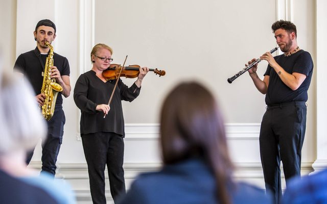 People watching a concert with a saxaphone, violin and clarinet in the concert hall