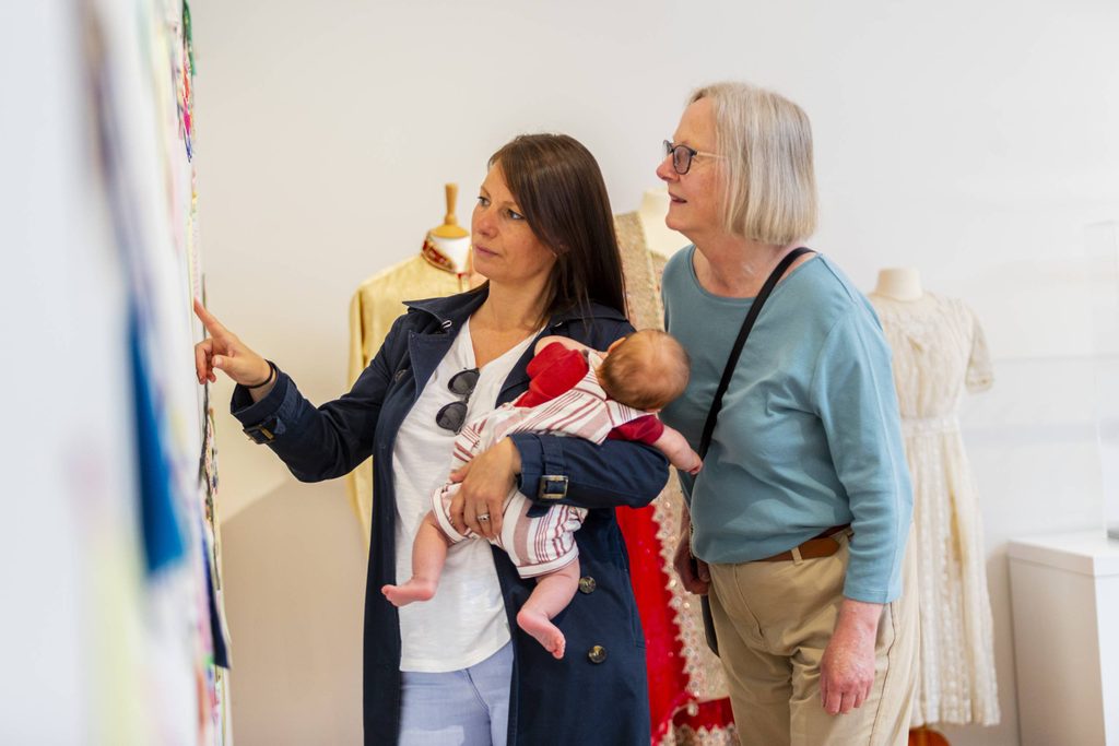 Two women look at the gallery display. One of them is holding a baby.