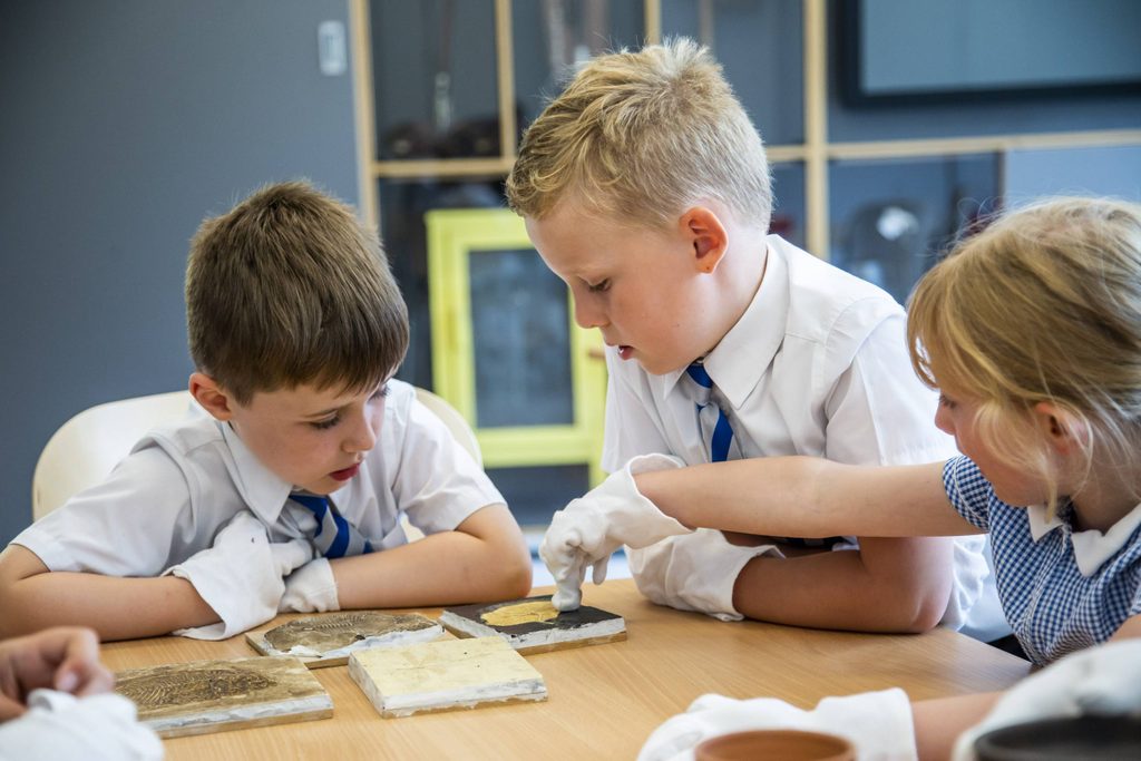 Three children handling museum objects whilst wearing white gloves