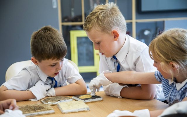 Three children handling museum objects whilst wearing white gloves