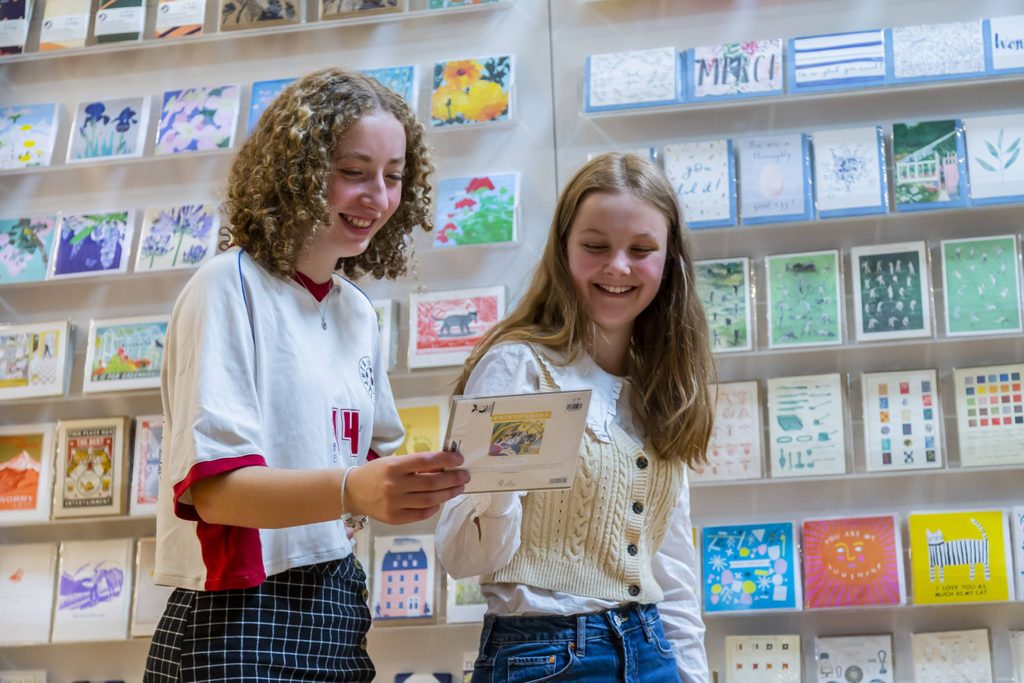 Two teenage girls looking at a greetings card and smiling.