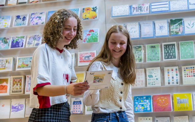 Two teenage girls looking at a greetings card and smiling.
