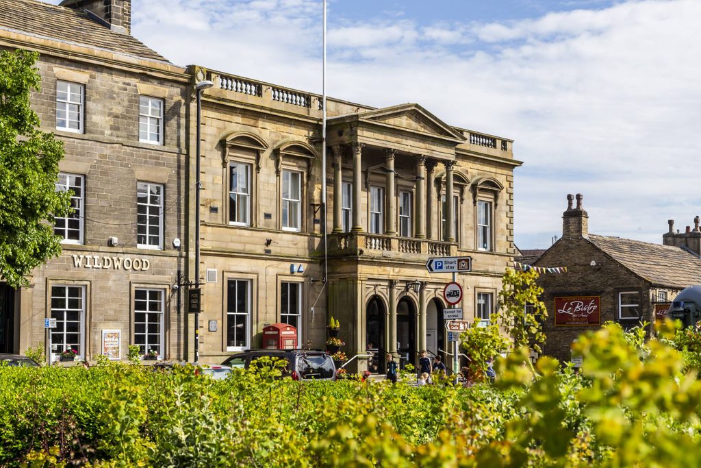 The extertior of Skipton Town Hall. Stone building with cgreen bush in the forground.