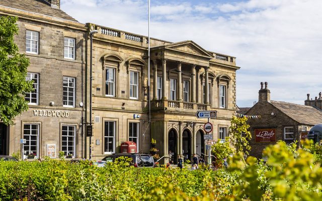 The extertior of Skipton Town Hall. Stone building with cgreen bush in the forground.