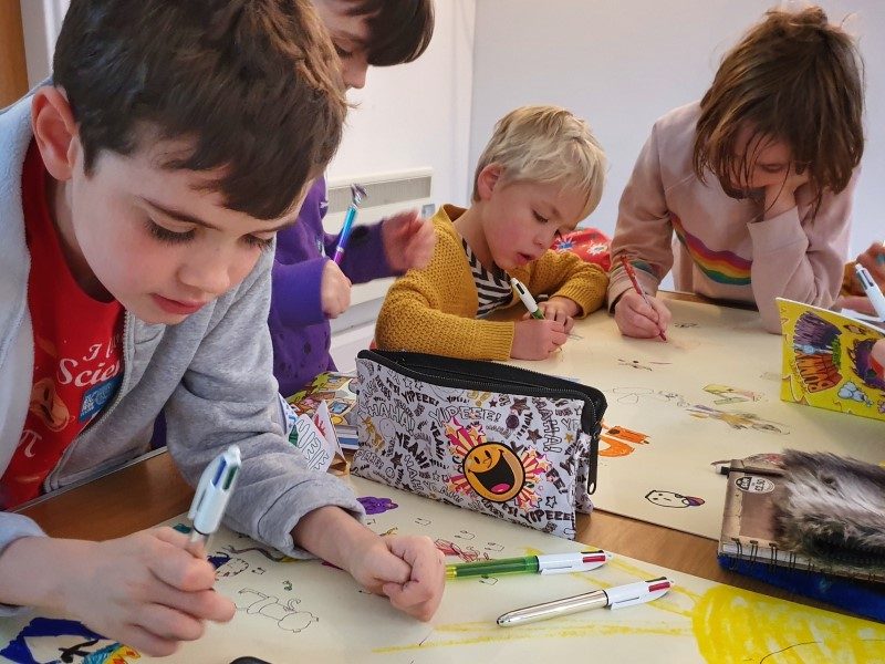 Four children drawing pictures on large pieces of paper.