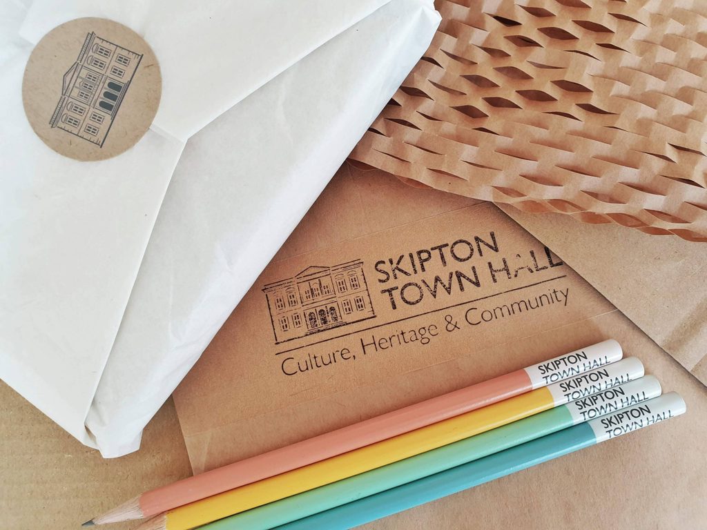 brown and white paper packaging with the Skipton Town Hall brnding and some coloured pencils.