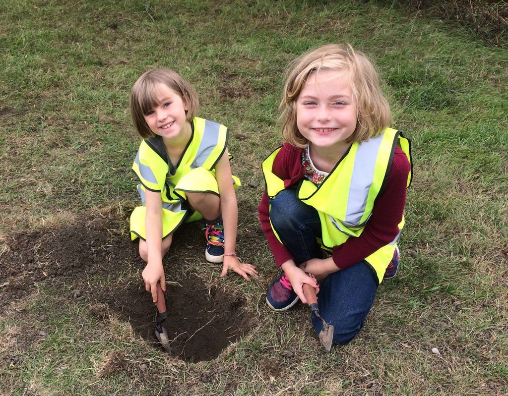Two girls in high visibility vests are digging in a field