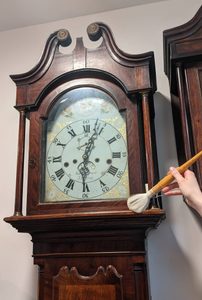 Han holding a large brush dusting a longcase clock