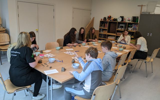 Young people sit round a large table. They are making things with clay.
