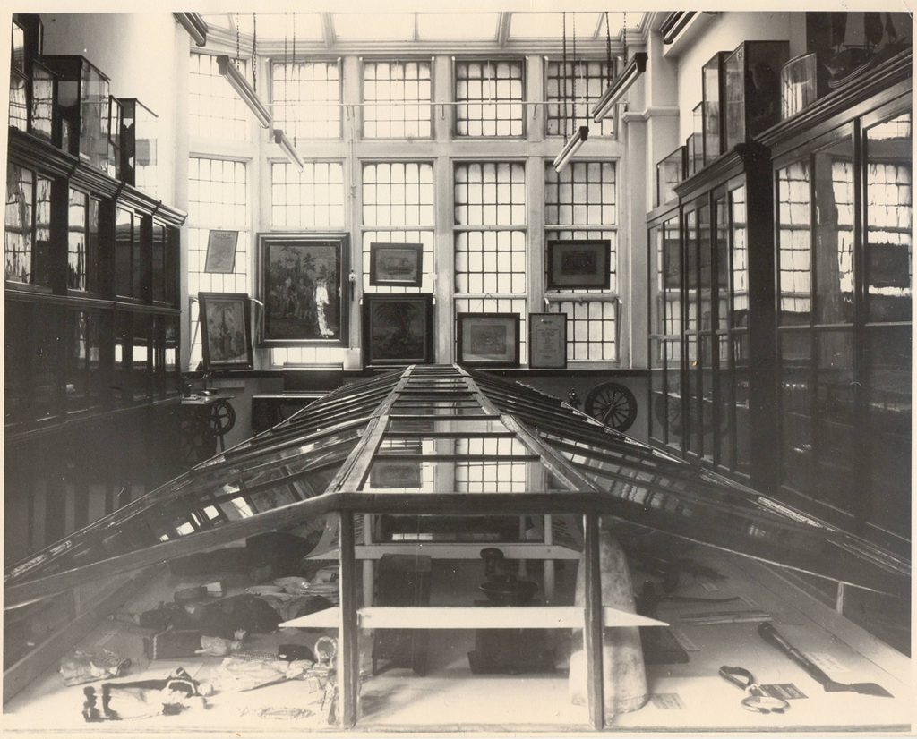 Black and white photo of wood and glass display cases in a windowed room