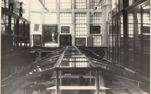 Black and white photo of wood and glass display cases in a windowed room